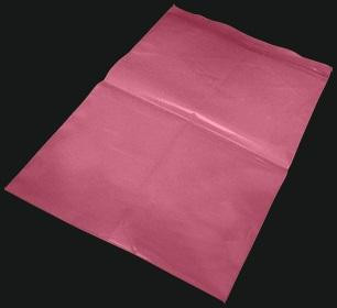 A large sheet of pink tissue paper is laid flat against a dark background, showing folds and creases.