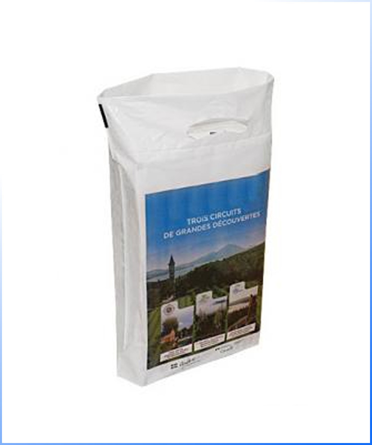 A white rectangular bag with a handle and a printed brochure on the front showing a landscape and text in French.