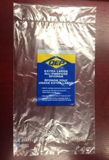 A clear empty plastic packaging labeled "QEP Extra Large All-Purpose Sponge" lies on a dark brown surface.