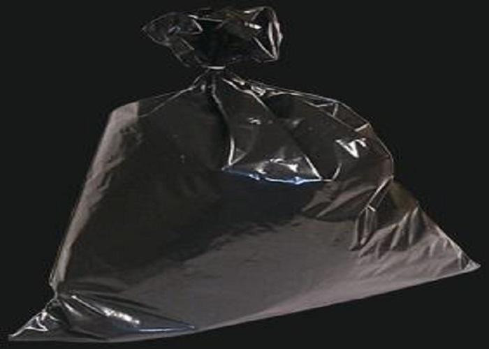 A full black plastic garbage bag tied at the top, set against a plain dark background.