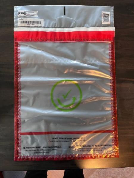 A large plastic mailing bag with a green checkmark symbol in the center, red sealing strips, and bilingual instructions printed along the top and bottom edges.