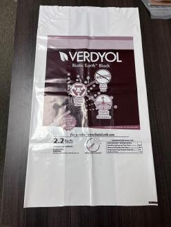 A white plastic bag labeled "VERD YOL Biotic Earth Black" with text, diagrams, and specifications printed on the front, lying flat on a dark surface.