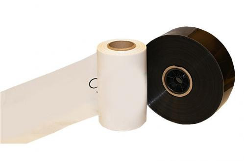 Two large rolls of plastic film, one white and one black, are positioned upright next to each other with some film unrolled from the white roll.