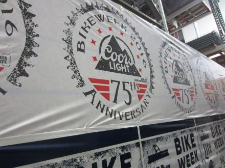 A banner displays the Coors Light logo and text reading "Bike Week 75th Anniversary" in a warehouse or industrial setting.