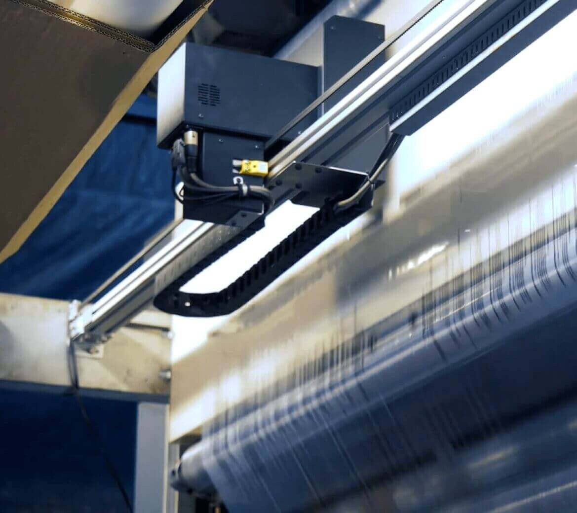 Close-up of an industrial textile manufacturing machine weaving fabric with threads visible on the moving loom.